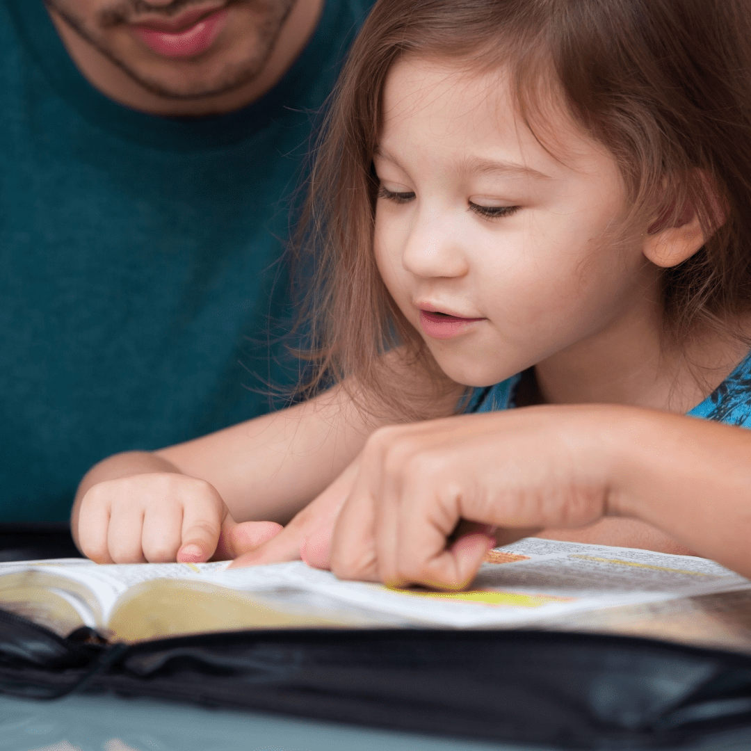 Child reading a book with adults